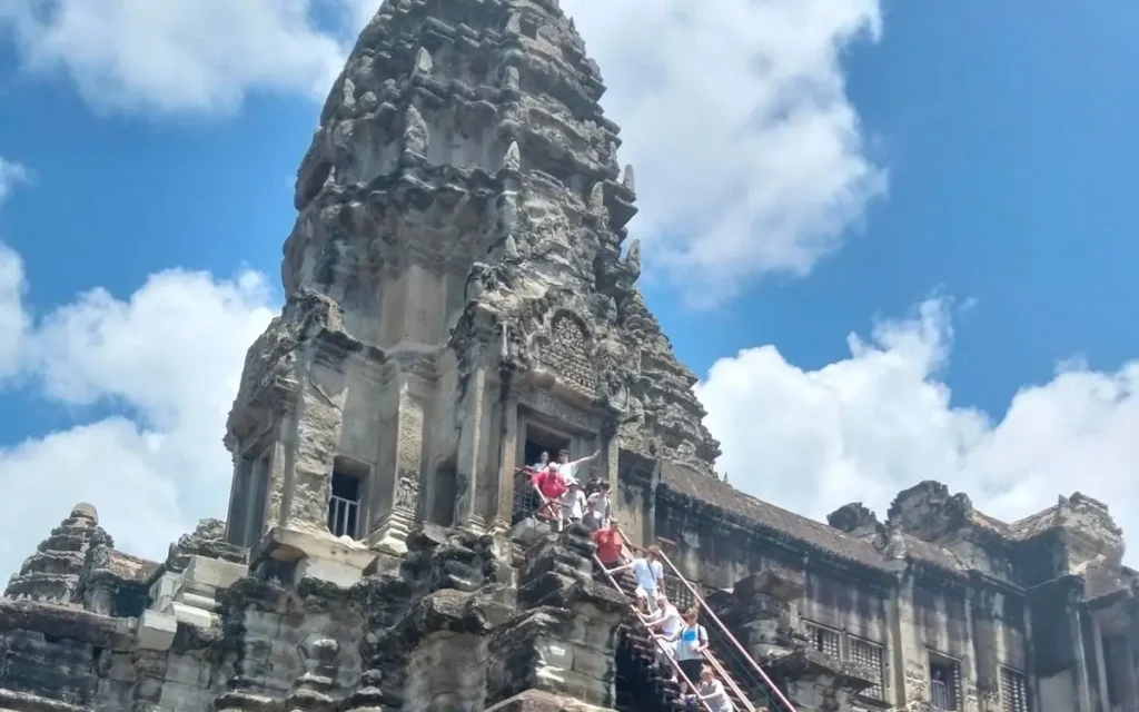 Visitors climbing the stone steps of an ancient Angkor Wat temple tower in Siem Reap, Cambodia