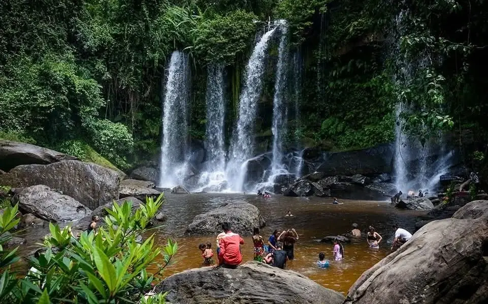 Visitors swimming beneath a waterfall surrounded by tropical forest at Phnom Kulen, Cambodia